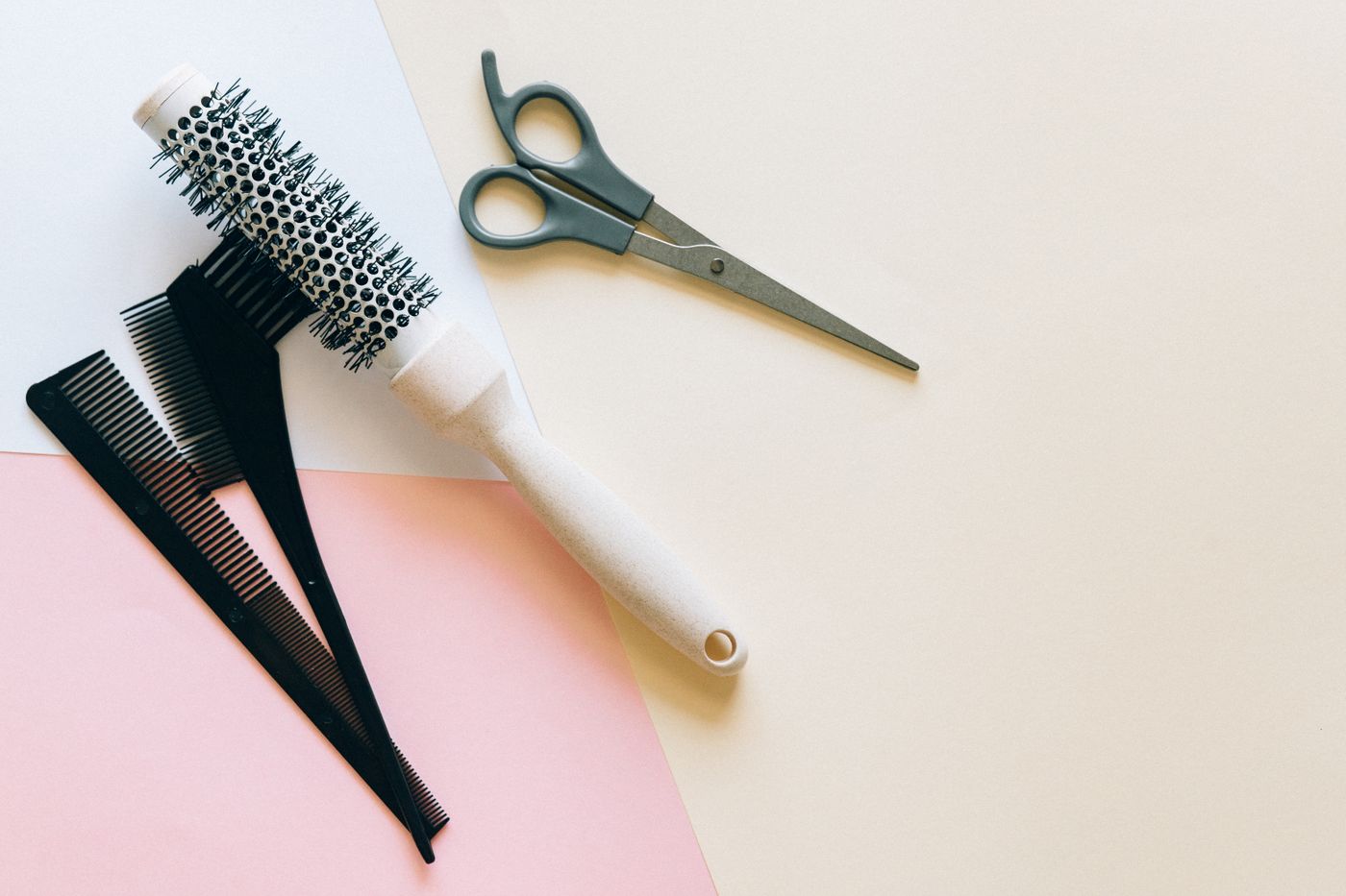 A round bristle brush, two black combs and a pair of grey-handled scissors on split pastel paper.